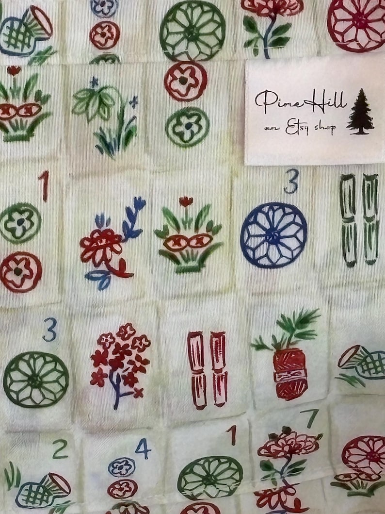 May include: Close-up of a fabric with a repeating pattern of Mahjong tiles. The tiles are white with colorful illustrations of flowers, circles, and bamboo. The text "Pine Hill an Etsy shop" is on a white label.