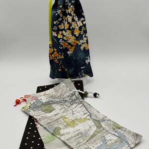 May include: Three drawstring bags made of fabric. The first bag is navy blue with a floral pattern. The second bag is white with a map pattern. The third bag is black with white polka dots.