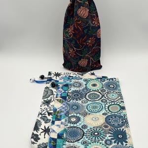 May include: A navy blue drawstring bag with a floral pattern, and three patterned pouches. The bag has a red drawstring. The pouches feature floral, geometric, and circular designs in shades of blue, white, and green.