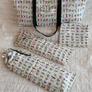 May include: A set of matching fabric items, including a tote bag, a small square pouch, and two long, cylindrical pouches. The items are white with a repeating pattern of colorful floral and geometric designs. The tote bag has dark green handles.