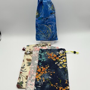 May include: Four drawstring bags with different floral patterns. The bags are made of fabric and have a drawstring closure. The bags are in various colors, including blue, cream, pink, and gray.