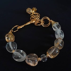 May include: A gold bracelet with a clasp and a chain. The bracelet is made with clear and amber colored stones.