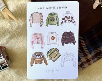 May include: A sheet of stickers featuring illustrations of cozy sweaters in various styles and colors, including a pink cardigan, a green sweater, and a sweater with a pumpkin design. The text "Cozy Sweater Weather" is at the top.