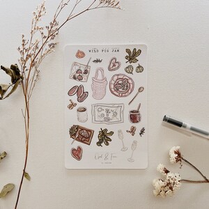 Può includere: Un foglio di adesivi con illustrazioni di marmellata di fichi selvatici, barattoli e altri articoli correlati. Gli adesivi sono su uno sfondo bianco e hanno uno stile disegnato a mano. Il testo "WILD FIG JAM" è in cima al foglio.
