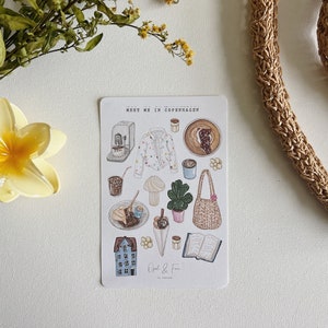 Pode incluir: Uma folha de adesivos com ilustrações de uma cafeteria em Copenhague, Dinamarca. A folha inclui imagens de café, doces, um prédio, uma bolsa e um livro. O texto na folha diz "Meet me in Copenhagen" e "Opal & Finn".