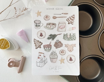 May include: A sheet of stickers featuring illustrations of winter baking themed items, including a gingerbread house, a mug of hot chocolate, a cupcake, and a star. The stickers are on a white background and have the text "Winter Baking" and "Opal & Fern" on them.