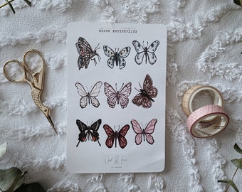 May include: A sheet of stickers featuring watercolor butterfly illustrations in various colors, including pink, brown, and black. The sheet is labeled "Blush Butterflies" and includes the text "Opal & Fern". Gold scissors and decorative tape rolls are also visible.