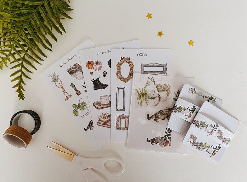 May include: A collection of decorative stickers and stationery featuring botanical and autumnal themes. The stickers include illustrations of plants, frames, cats, and seasonal elements. Also included are washi tape rolls and a pair of scissors.
