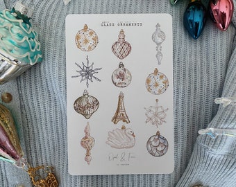 May include: A sheet of stickers featuring 12 illustrated vintage glass ornaments. The ornaments are in various shapes and colors, including gold, white, and pink. The stickers are labeled "Glass Ornaments" and "Opal & Fern by Kristen".
