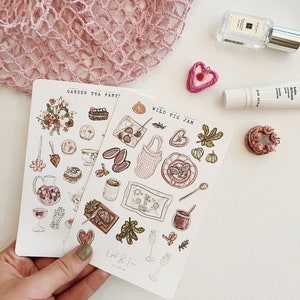 May include: Two sets of stickers featuring illustrations of food and drinks. The first set is titled "Garden Tea Party" and features a teapot, teacups, pastries, and flowers. The second set is titled "Wild Fig Jam" and features figs, jam, bread, and wine glasses.