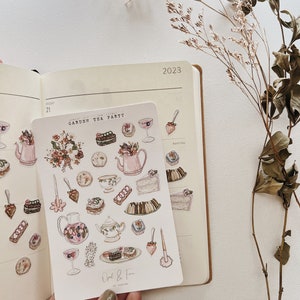 May include: A sheet of stickers featuring watercolor illustrations of tea party elements, including teacups, teapots, cakes, pastries, and flowers. The stickers are labeled "Garden Tea Party" and "Opal & Fern by Sophie".
