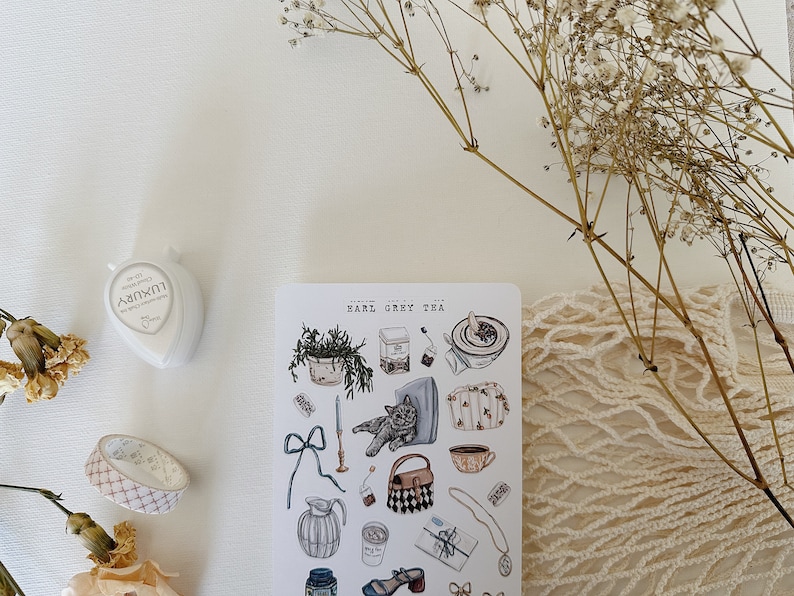 May include: A sheet of stickers with illustrations of teacups, teapots, a cat, a potted plant, and other tea-related items. The stickers are on a white background and have a vintage aesthetic. The text "Earl Grey Tea" is printed at the top of the sheet.