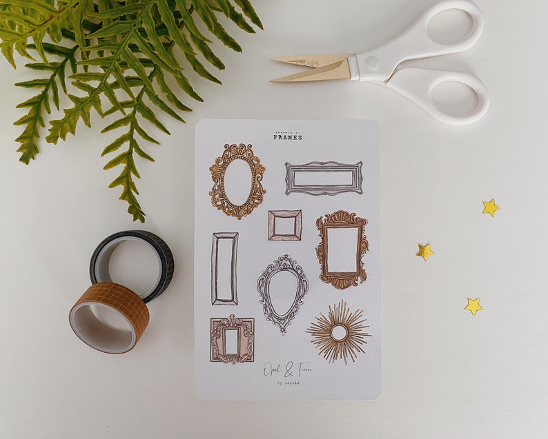 May include: A sticker sheet featuring various frame designs in gold and brown tones, with the text "FRAMES" at the top. The image includes washi tape, scissors, fern leaves, and gold star-shaped confetti.