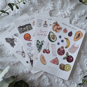 Peut inclure: Quatre feuilles d'autocollants avec diverses illustrations. La premi&egrave;re feuille repr&eacute;sente un papillon, un b&acirc;timent, une tasse &agrave; th&eacute;, une &eacute;chelle et un oiseau. La deuxi&egrave;me feuille repr&eacute;sente un fruit, une grenade, une cerise, un kiwi, une past&egrave;que et un re&ccedil;u. La troisi&egrave;me feuille repr&eacute;sente une papaye, une banane, une figue, une p&ecirc;che, un avocat et un sac en filet. La quatri&egrave;me feuille repr&eacute;sente un b&acirc;timent, une tasse &agrave; th&eacute;, une plante et le texte "love lives her".