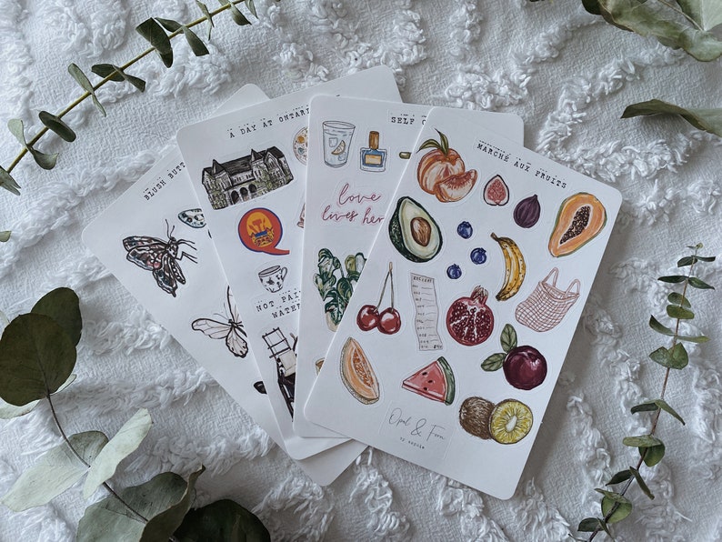 Peut inclure: Quatre feuilles d'autocollants avec diverses illustrations. La premi&egrave;re feuille repr&eacute;sente un papillon, un b&acirc;timent, une tasse &agrave; th&eacute;, une &eacute;chelle et un oiseau. La deuxi&egrave;me feuille repr&eacute;sente un fruit, une grenade, une cerise, un kiwi, une past&egrave;que et un re&ccedil;u. La troisi&egrave;me feuille repr&eacute;sente une papaye, une banane, une figue, une p&ecirc;che, un avocat et un sac en filet. La quatri&egrave;me feuille repr&eacute;sente un b&acirc;timent, une tasse &agrave; th&eacute;, une plante et le texte "love lives her".