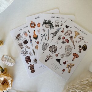 May include: Four sheets of stickers with various illustrations. The stickers are on a white background. The stickers feature illustrations of coffee, tea, apples, and mushrooms. The text on the stickers reads "9 AM Coffee", "Earl Grey Tea", "Apple", and "Forest Foraging".