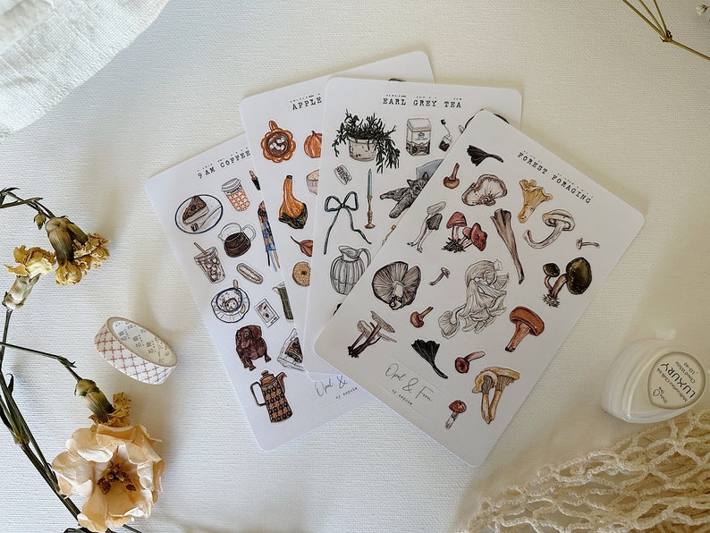 May include: Four sheets of stickers with various illustrations. The stickers are on a white background. The stickers feature illustrations of coffee, tea, apples, and mushrooms. The text on the stickers reads "9 AM Coffee", "Earl Grey Tea", "Apple", and "Forest Foraging".