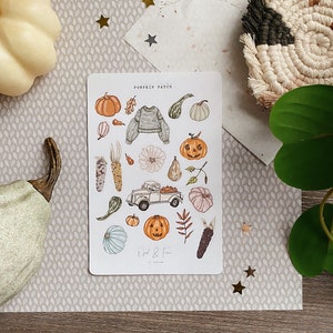 Può includere: Un foglio di adesivi a tema autunnale. Gli adesivi raffigurano zucche, zucche, un camioncino vintage, un maglione e mais. Il foglio è intitolato "Pumpkin Patch".