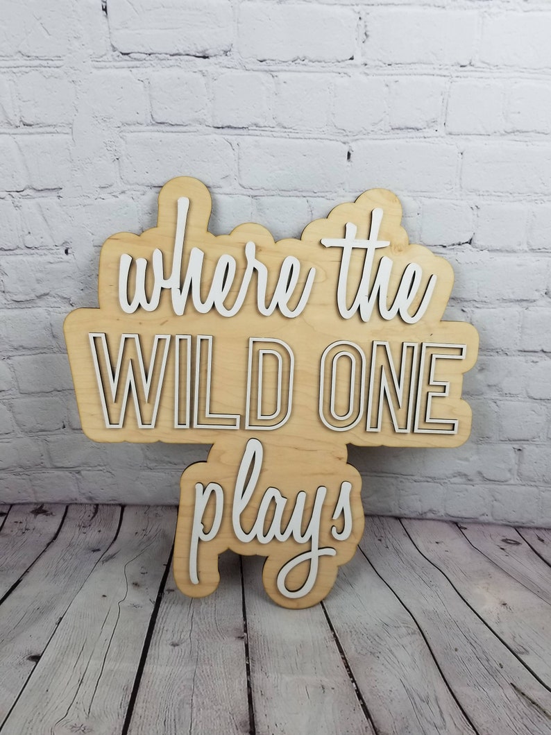 Op de afbeelding: Een houten bord met de tekst "Where the Wild One Plays" in witte letters. Het bord is gemaakt van licht hout en heeft een rustieke uitstraling.