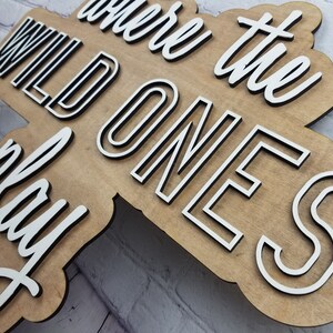 Op de afbeelding: Een houten bord met de tekst "Where the Wild Ones Play" in witte letters met zwarte contouren. Het bord is gemaakt van lichtbruin hout en heeft een rustieke uitstraling.