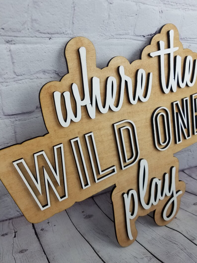 Op de afbeelding: Houten bord met de tekst "Where the Wild Ones Play" in witte letters met zwarte contouren.