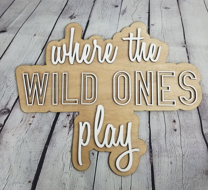 Op de afbeelding: Een houten bord met de tekst "Where the Wild Ones Play" in witte letters. Het bord is gemaakt van lichtbruin hout en heeft een rustieke uitstraling.