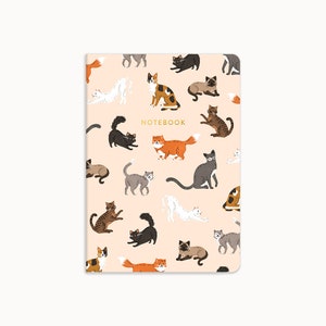 May include: A pink notebook featuring a pattern of colourful cats in various poses. The notebook says "NOTEBOOK" in gold lettering.