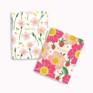May include: Two floral patterned notebooks with the word "NOTES" in gold lettering on the front cover. One notebook has a pink and white floral pattern, and the other has a pink and green floral pattern with strawberries.