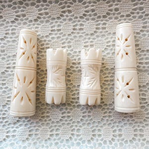 May include: Four off-white cylindrical objects with carved details. The two outer pieces are taller with star-shaped cutouts, while the two inner pieces are shorter with crenelated tops and leaf-like carvings. All items feature horizontal grooves.