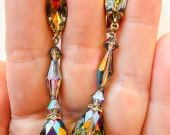 May include: A pair of long dangle earrings featuring faceted, iridescent crystals in shades of amber, green, and purple. Each earring consists of a marquise-shaped top stone connected to a series of smaller beads and a large, teardrop-shaped base.