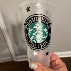 May include: A clear plastic reusable cup with a black and white design featuring the Starbucks logo and the text "PROVIDENCE COLLEGE". The cup has silver glitter and white and black stars.