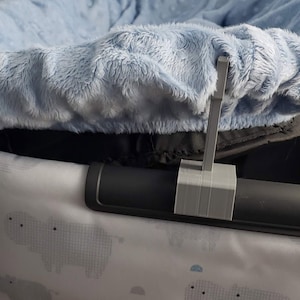 May include: A close-up of a gray plastic clip attached to a black metal bar. The clip is holding a light blue fabric cover in place. The fabric cover is made of a soft, fuzzy material.