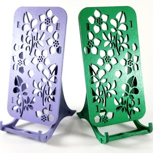 May include: Two wooden phone stands with a floral design. One stand is purple and the other is green.