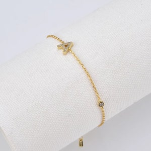 Könnte beinhalten: Ein goldenes Kettenarmband mit einem Buchstaben A-Anhänger und einem kleinen klaren Kristall. Der Anhänger ist mit kleinen klaren Kristallen besetzt.