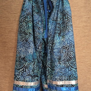 May include: A long, loose-fitting skirt featuring a blue and black paisley pattern. The garment includes a blue ribbon drawstring at the waist and two horizontal ribbon stripes near the hem, one in silver and one in a vibrant royal blue color.