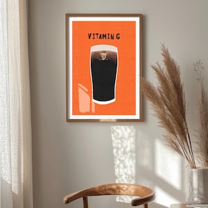 Peut inclure: Une affiche encadr&eacute;e repr&eacute;sentant une pinte de stout fonc&eacute; avec une t&ecirc;te cr&eacute;meuse sur fond orange. Le texte "VITAMIN G" est imprim&eacute; au-dessus de la pinte. L'affiche est accroch&eacute;e au mur dans une pi&egrave;ce.