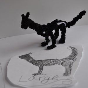 May include: A black pipe cleaner dragon sculpture with white accents. The dragon is posed on a white surface with a pencil drawing of a larger dragon underneath it. The drawing is labeled "Large".
