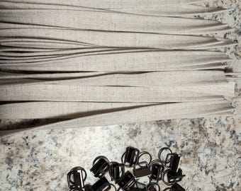 Puede incluir: Un montón de hebillas deslizantes de metal negro con anillas en D. Las hebillas están dispuestas de forma aleatoria sobre una superficie gris claro. Hay una pila de tiras de tela beige en el fondo.