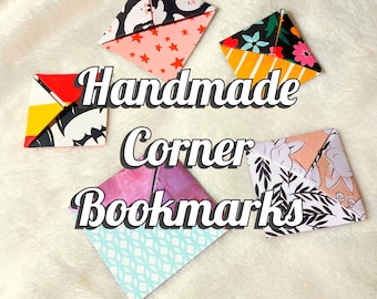 May include: Handmade corner bookmarks in various patterns, including bats, stars, flowers, and geometric designs. The text "Handmade Corner Bookmarks" is displayed in a cursive font. The bookmarks are made of folded paper.