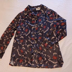 May include: A dark navy blue button-down shirt with a floral pattern. The long-sleeved shirt features large white and red flowers. The shirt has a collar and buttoned cuffs. The label reads "Gold Mountain".