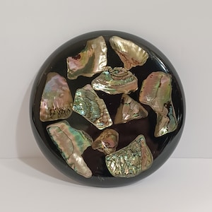 May include: A round black coaster with a decorative design of iridescent abalone shell pieces.