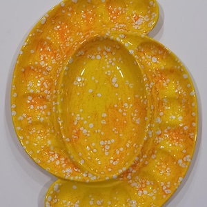 May include: A yellow ceramic serving dish with an oval center and two curved side sections. The dish has an orange speckled pattern with white dots. The dish is likely vintage and suitable for serving snacks or appetizers.