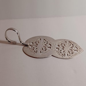 May include: A silver-colored cake server with an ornate, openwork design. The server features a handle with a curved end and a wide, oval-shaped blade with intricate floral patterns. The overall design is elegant and decorative.
