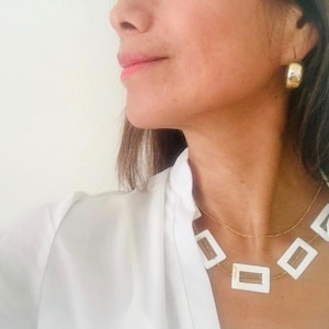May include: A gold hoop earring and a gold necklace with white rectangular pendants are visible. The necklace has a delicate gold chain. The person is wearing a white collared shirt.