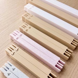 May include: A collection of rectangular, interlocking plastic bars in various colors including white, beige, light pink, and light blue. Each bar features a numerical label from 4 to 10 embossed on one end, with notched ends for assembly.