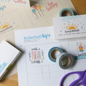 May include: A collection of birthday-themed stationery and craft supplies. Includes printed cards with "Happy Birthday" text, washi tape rolls, and a pair of purple scissors. The design features a sun and cake.