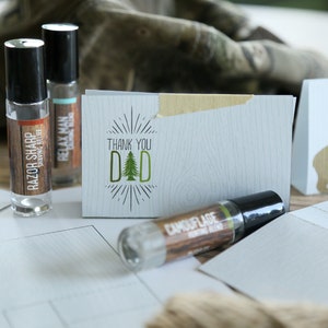 May include: An assortment of gifts for Dad, including shaving relief roll-on bottles and greeting cards. The cards feature text like "Thank You Dad" and "Love You Papa Bear". The roll-on bottles have labels that read "Razor Sharp" and "Camouflage".