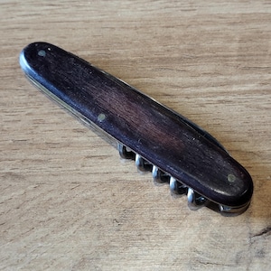 May include: A dark brown wooden handled pocket knife with a corkscrew and other tools.