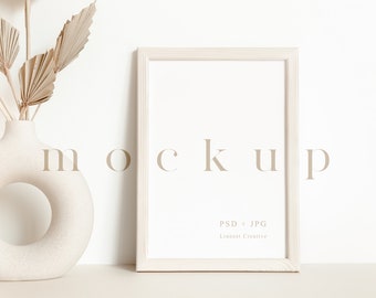 May include: A white frame mockup with a white vase with a hole in the middle and dried palm leaves. The text "MOCKUP" is written in a light brown font below the frame. The text "PSD + JPG" and "License Creative" is written in a light brown font at the bottom of the frame.
