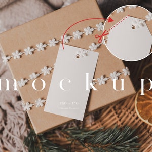 Puede incluir: Una caja de regalo marrón envuelta con encaje blanco y dos etiquetas de regalo en blanco. La caja está sentada en una cesta tejida con rodajas de naranja secas.